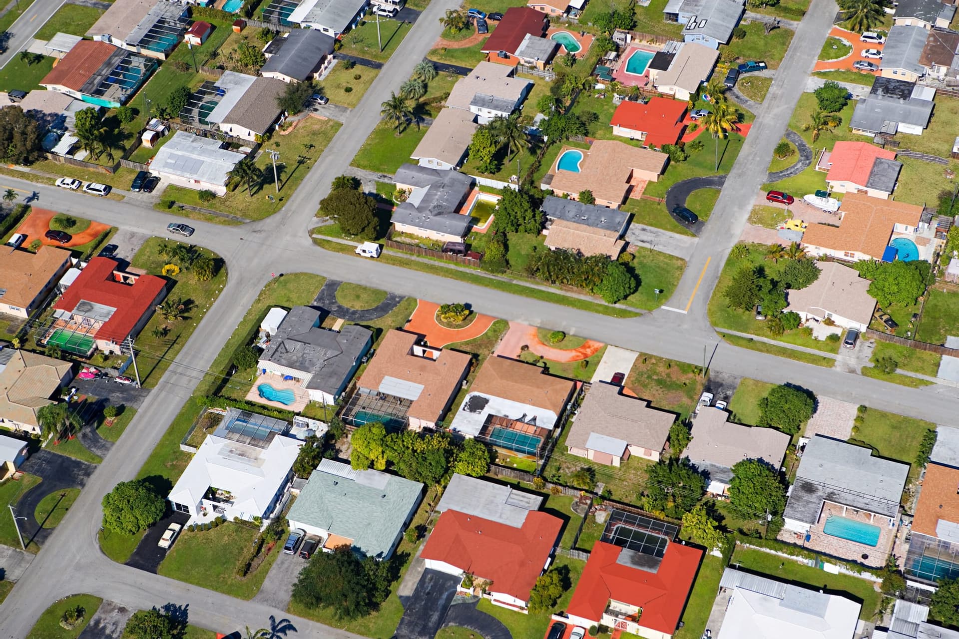 Aerial view of a waterfront neighborhood of single-story homes with pools and colorful roofs