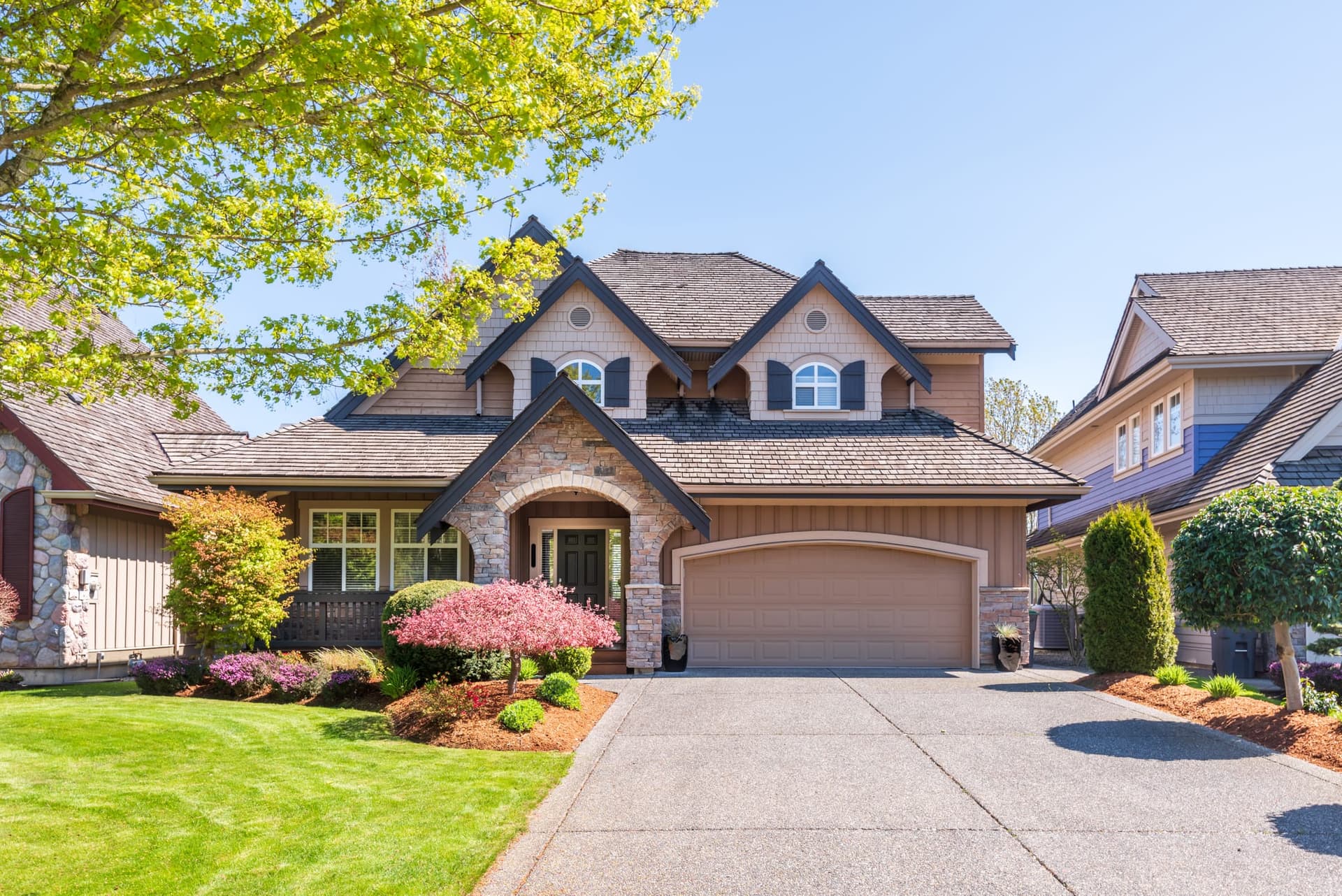 A large suburban home with a landscaped front yard, flowering shrubs and a wide driveway