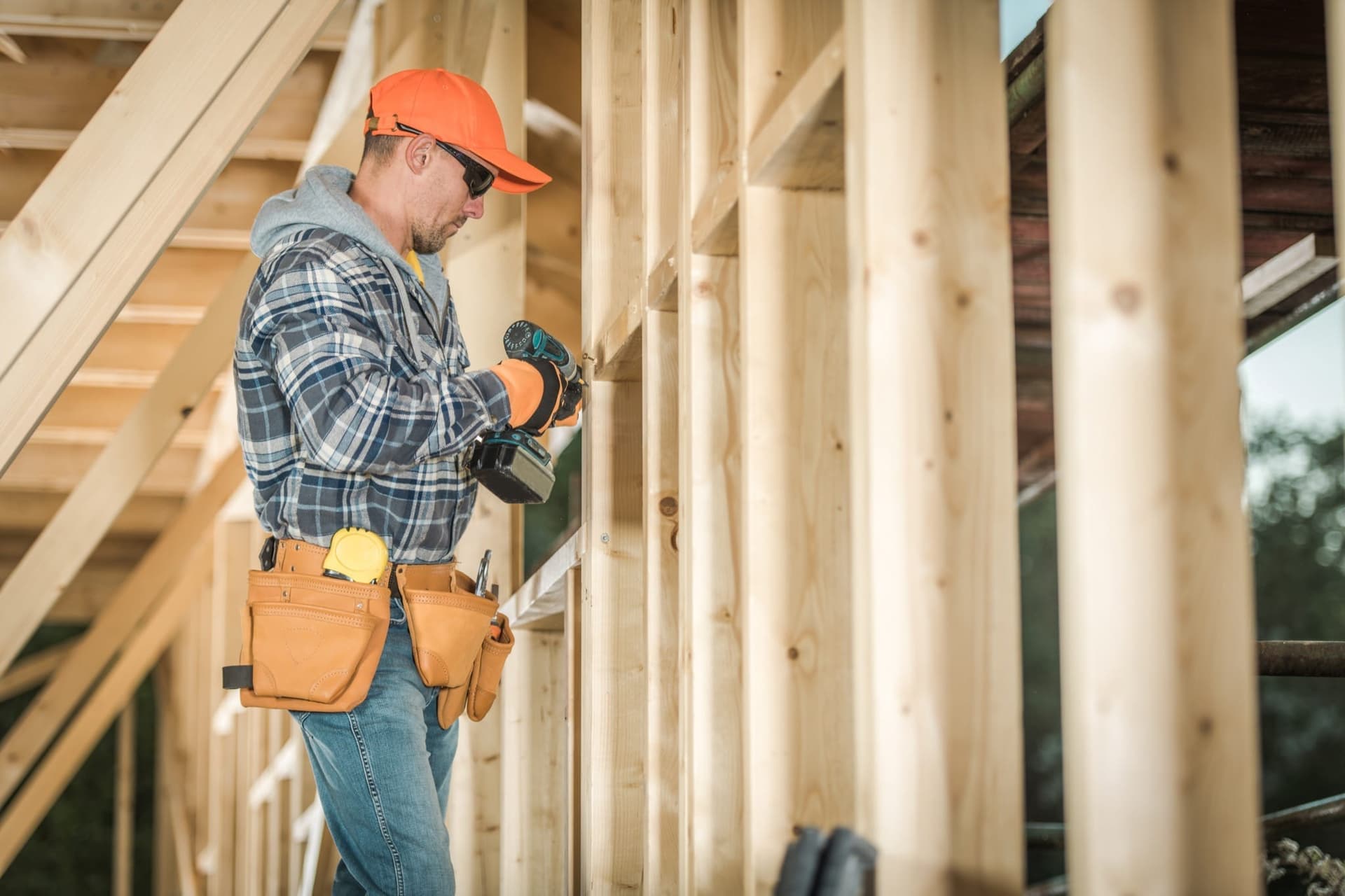 A contractor in a hard hat driving a screw with a power driver inside a timber-framed structure