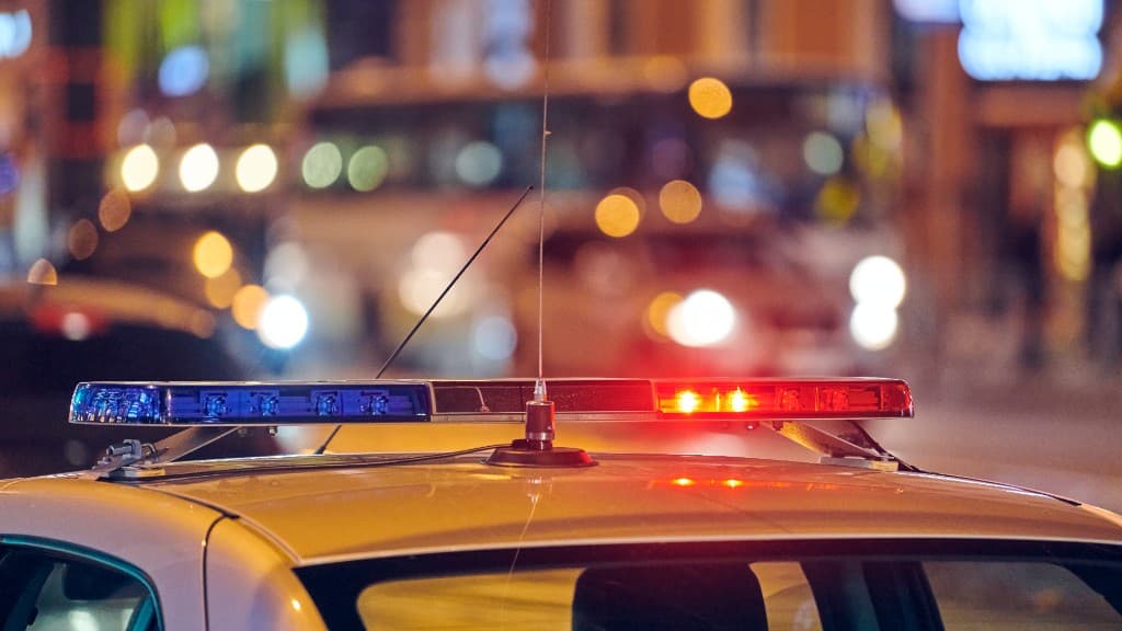 The illuminated red and blue light bar on a police car at night, city lights blurred behind it