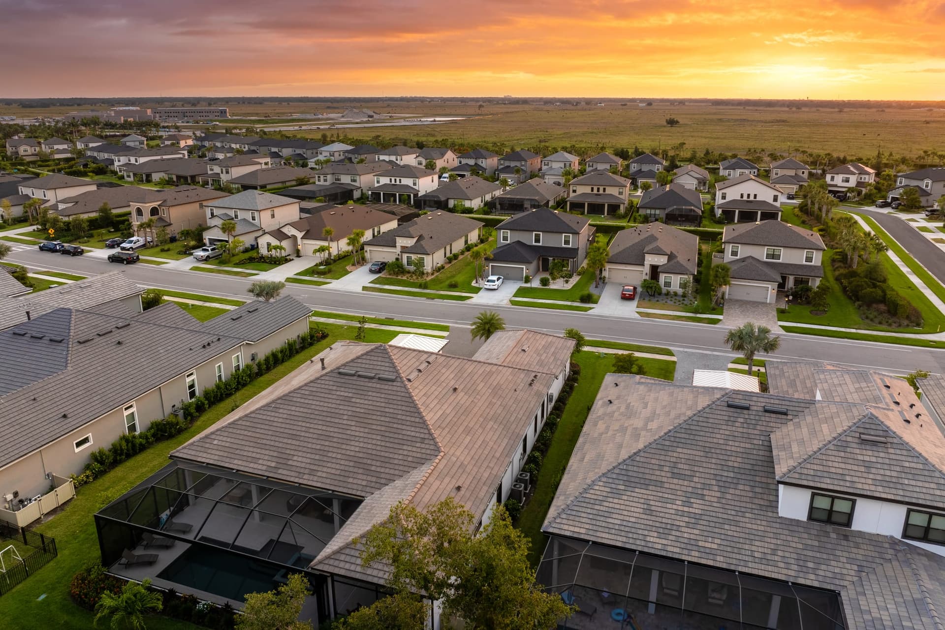 Aerial view at sunset over a newly built subdivision, hip roofs and screened pool enclosures in the foreground
