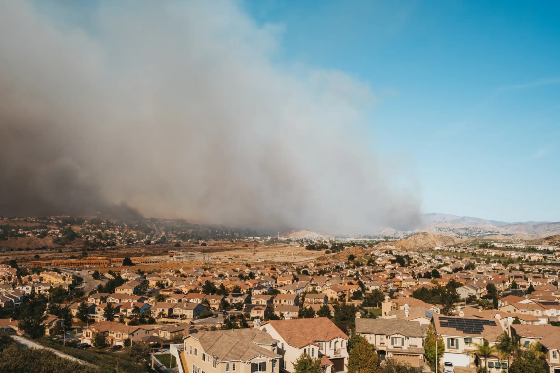 A wall of wildfire smoke rising over the hillsides above a residential subdivision